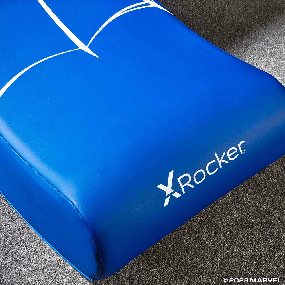 Blaues X-Rocker-Spielkissen mit weißem Design auf Teppichboden.