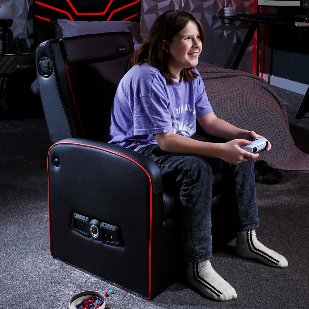 Ein Junge sitzt in einem schwarzen Gaming-Stuhl und spielt mit einem Controller.