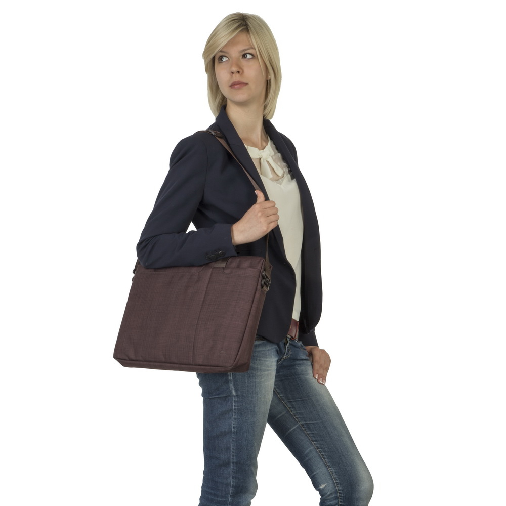 Une femme blonde porte un blazer bleu marine, un jean et un sac bandoulière marron.