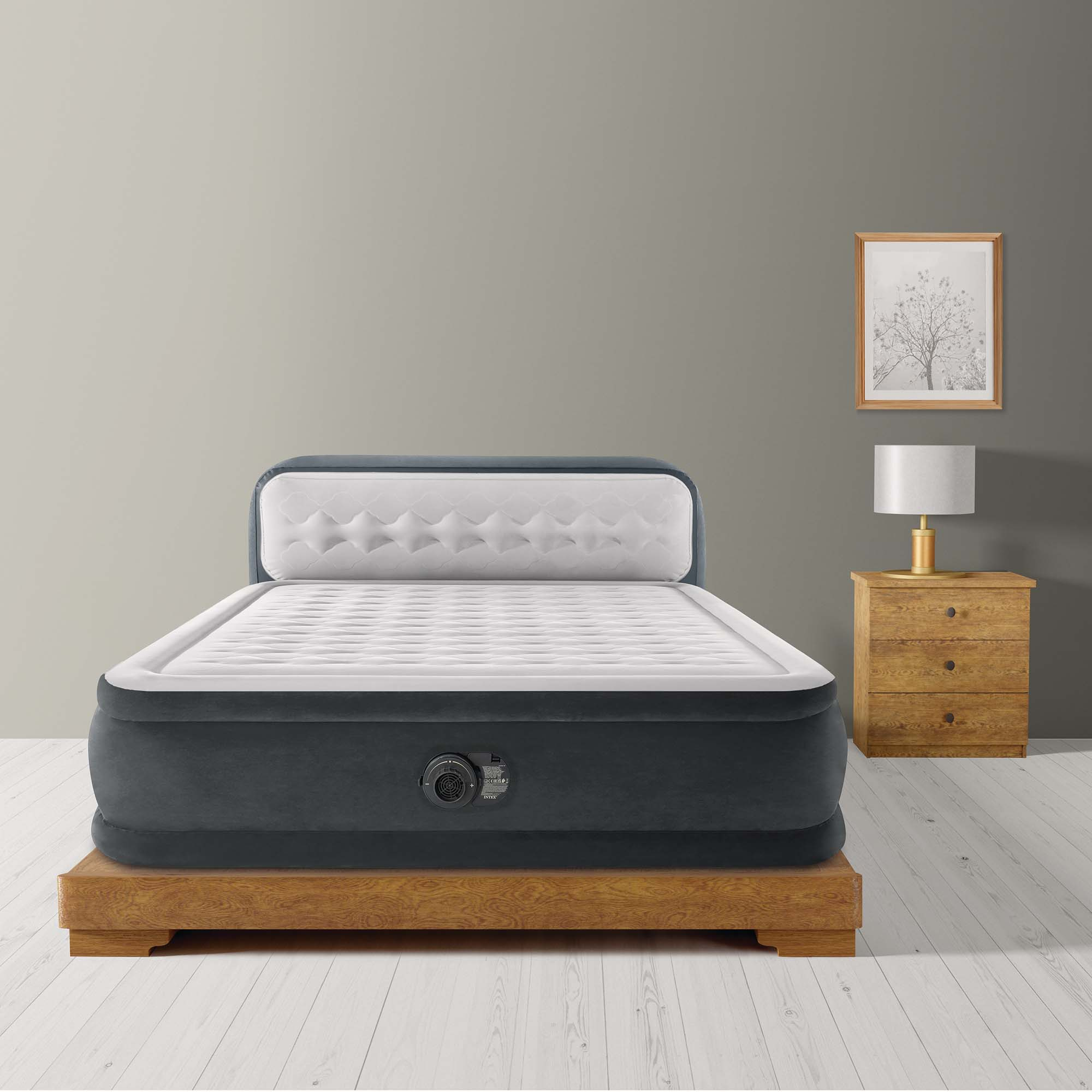 Una cama inflable descansa sobre una base de madera junto a una mesita de noche y una lámpara.