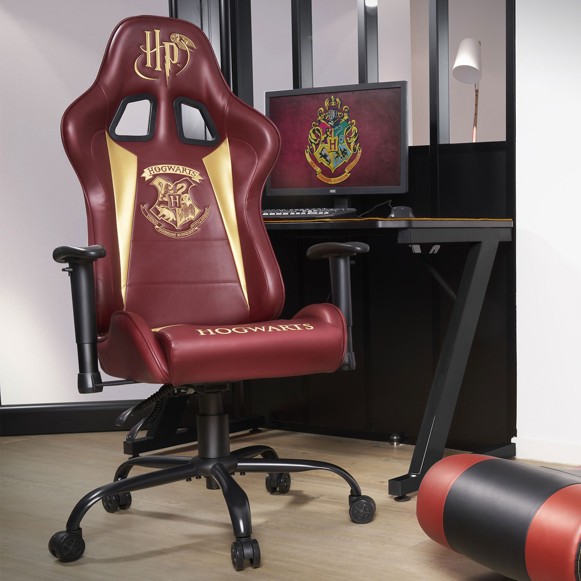 Ein burgunderroter Gaming-Stuhl mit Hogwarts-Logo und ein Schreibtisch mit Monitor.