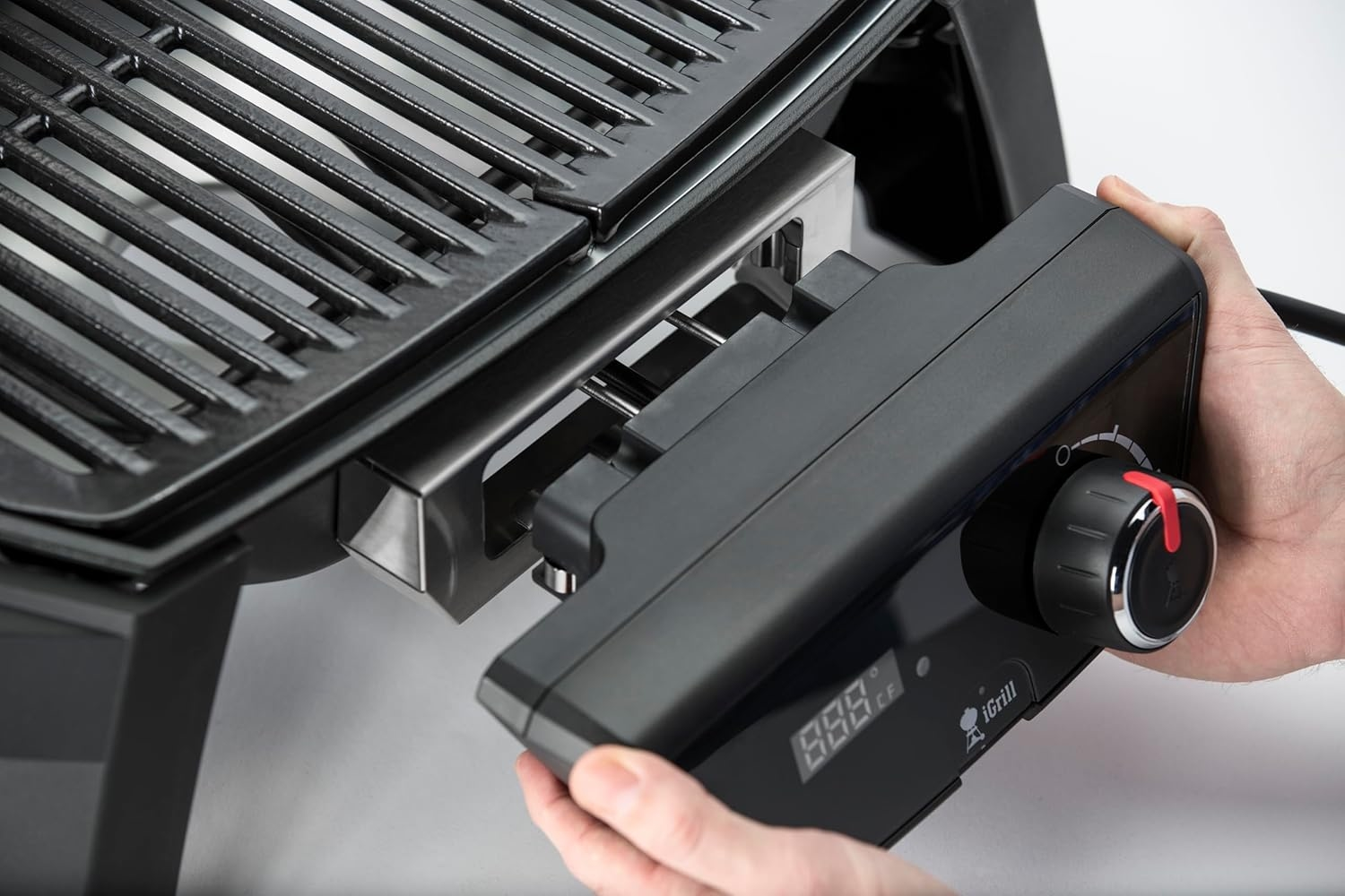 Hände montieren ein schwarzes Grillmodul mit Digitalanzeige und Drehknopf.