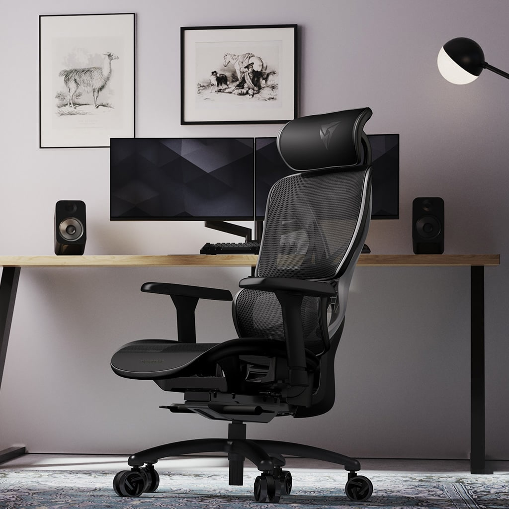 Una silla gamer negra se sitúa frente a un escritorio con dos monitores y altavoces.