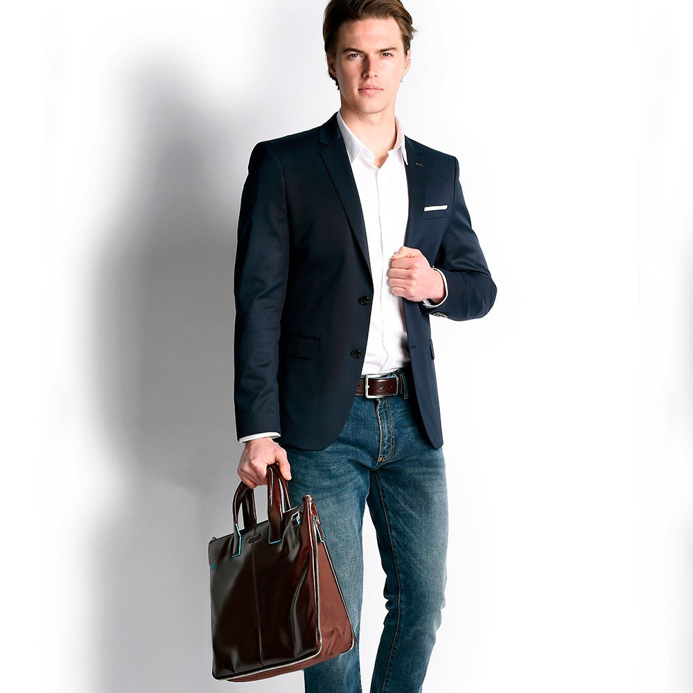 Ein Mann im dunklen Sakko, weißem Hemd, Jeans und brauner Tasche.