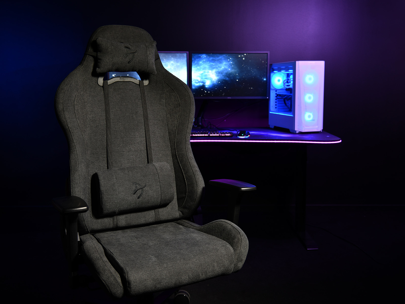 Een grijze gamestoel staat voor een bureau met twee monitoren, een pc en RGB-verlichting.