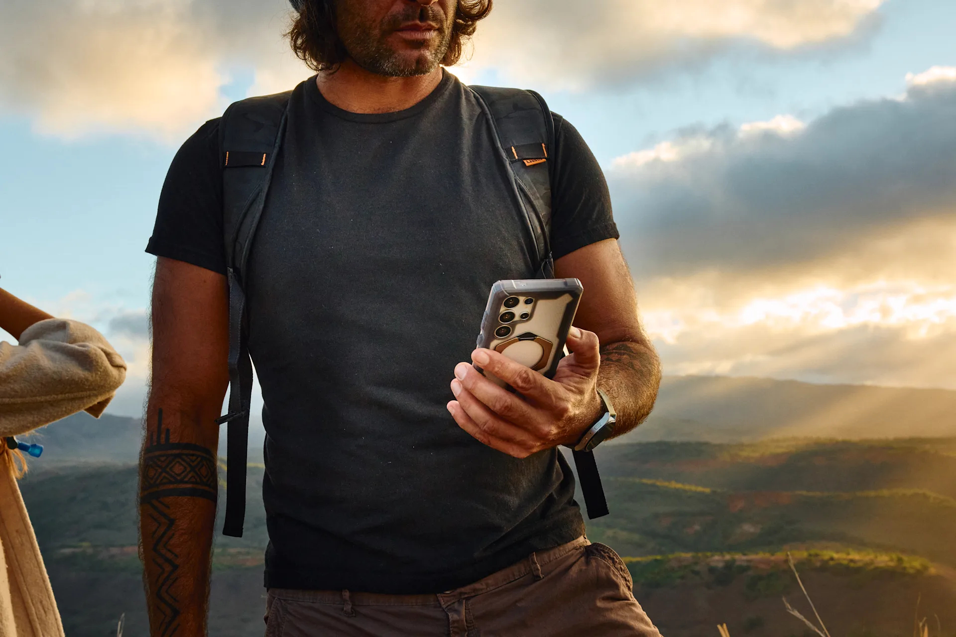 Uomo con zaino tiene telefono su belvedere montano con cielo nuvoloso.