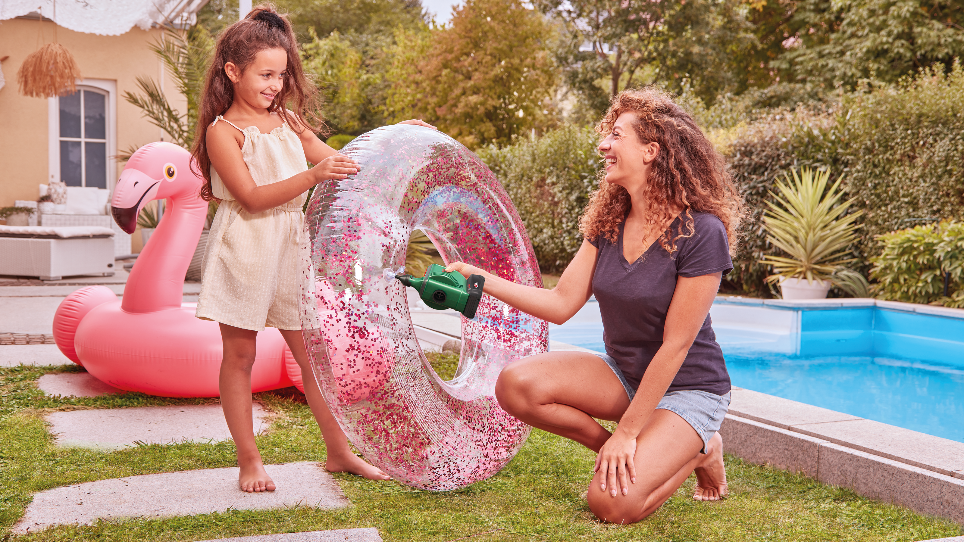 Matka pompująca pierścień z brokatem, córka i flaming w tle.