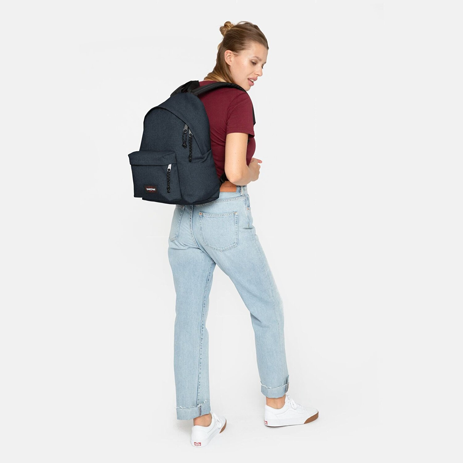 Frau mit dunkelblauem Rucksack, rotem Oberteil und Jeans. Weiße Sneaker.