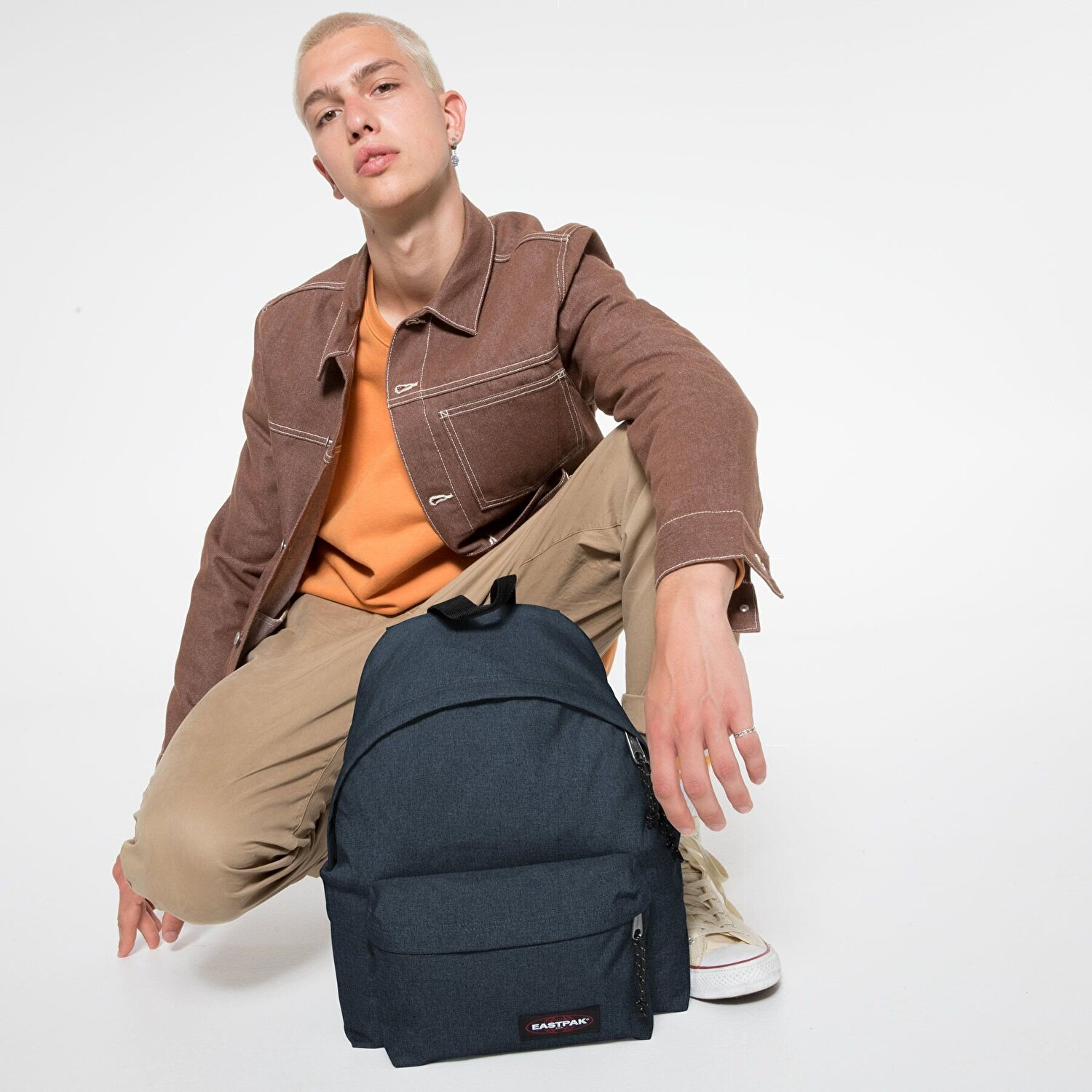 Ein Mann mit blonden Haaren kniet neben einem dunkelblauen Rucksack.