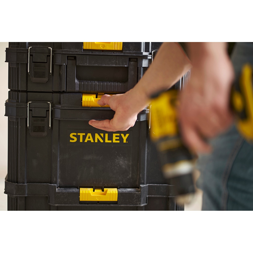 Ein Mann öffnet eine schwarze Stanley-Werkzeugkiste mit gelben Griffen.