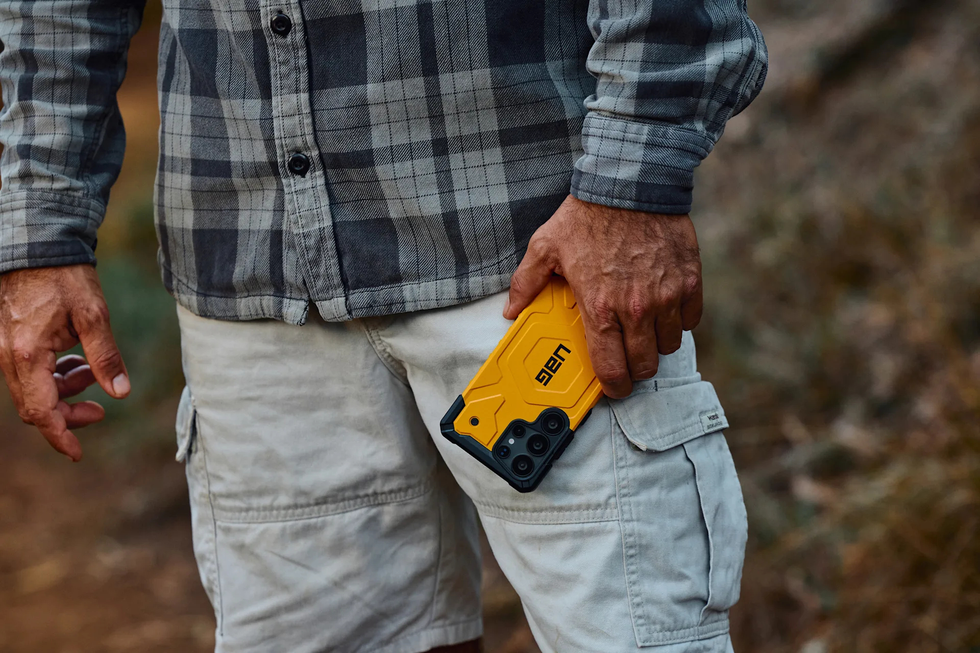 Uomo in camicia a quadri tiene uno smartphone giallo con custodia nera.