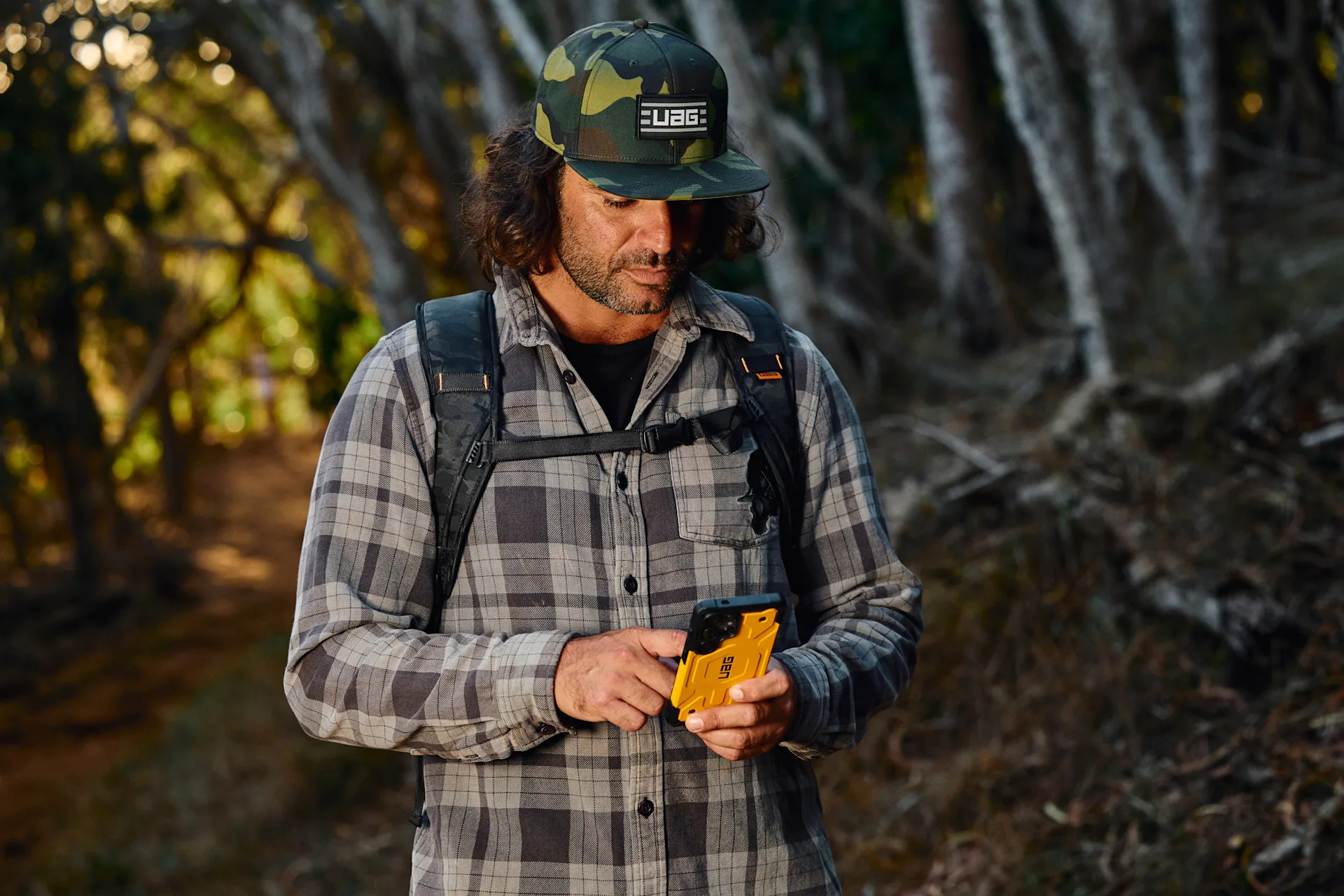 Uomo con cappellino mimetico e camicia a quadri tiene telefono giallo.