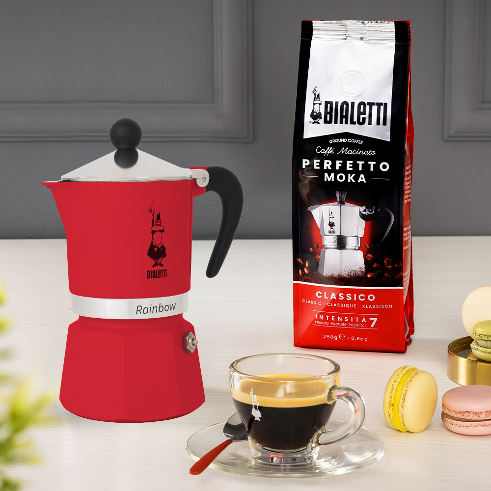 Rote Bialetti Kaffeemaschine, Kaffeebeutel, Espressotasse und Macarons.