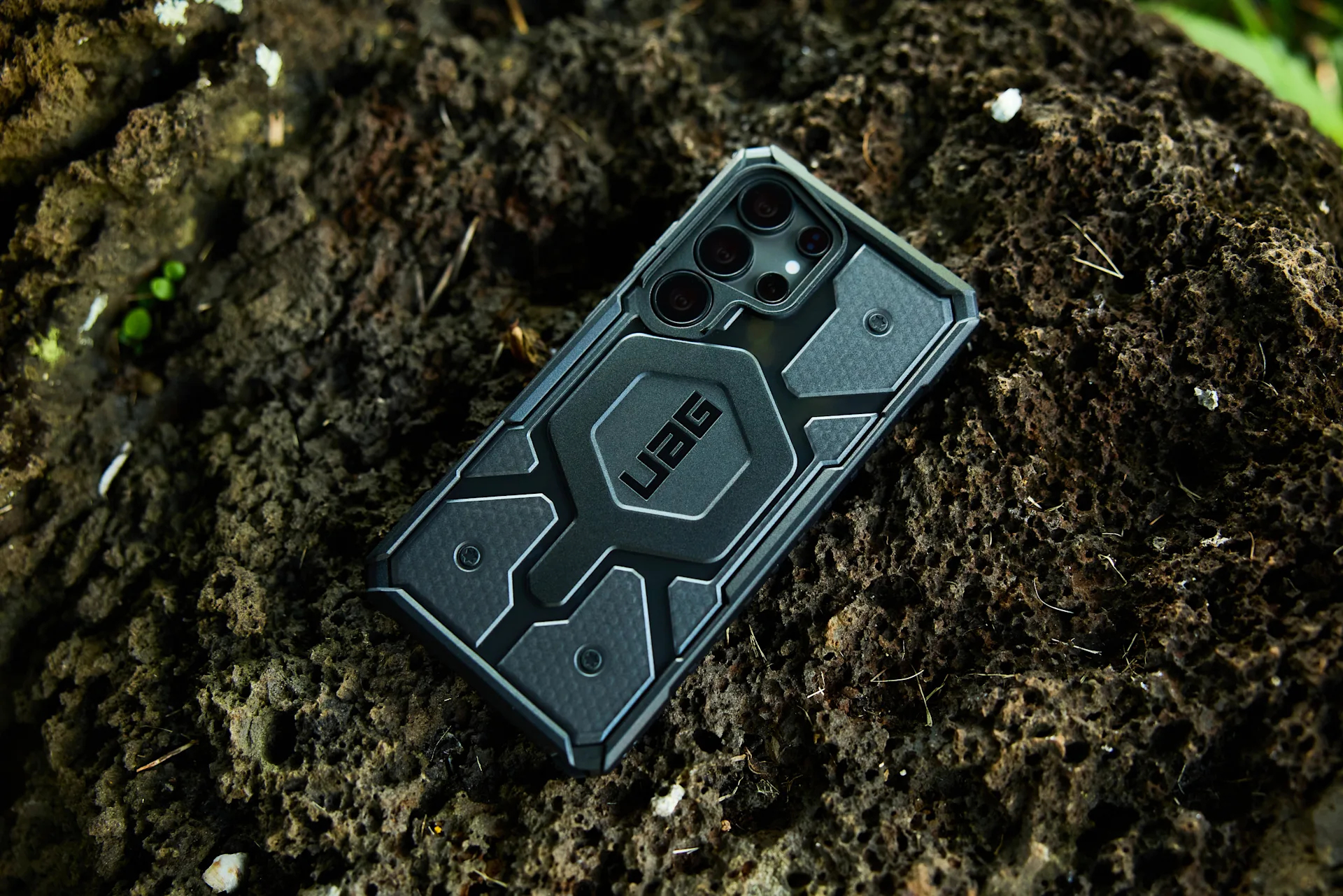 Custodia nera per telefono con logo "UAG" su sfondo scuro e ruvido.