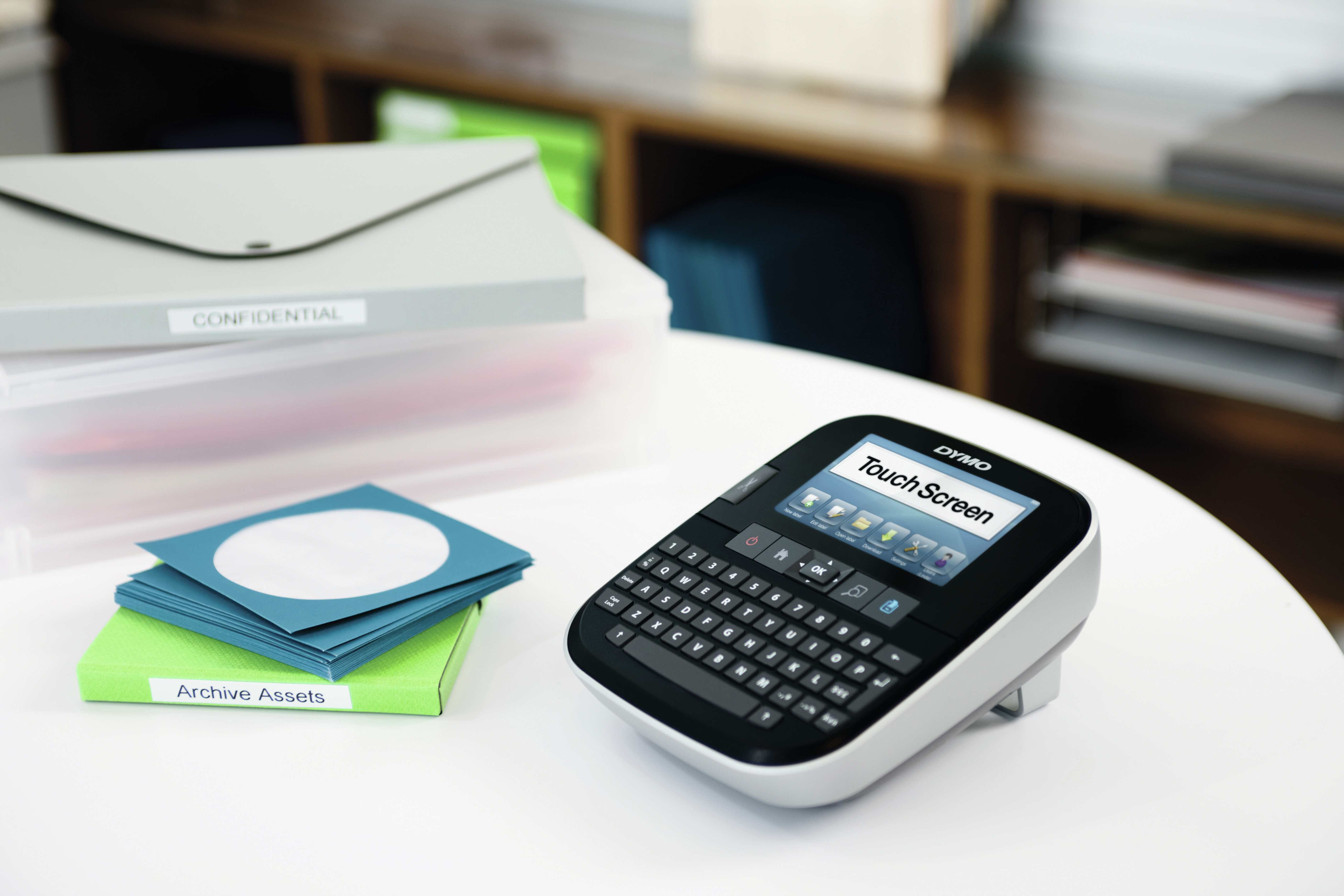 Una etichettatrice DYMO con touchscreen è su un tavolo vicino a cartelle.