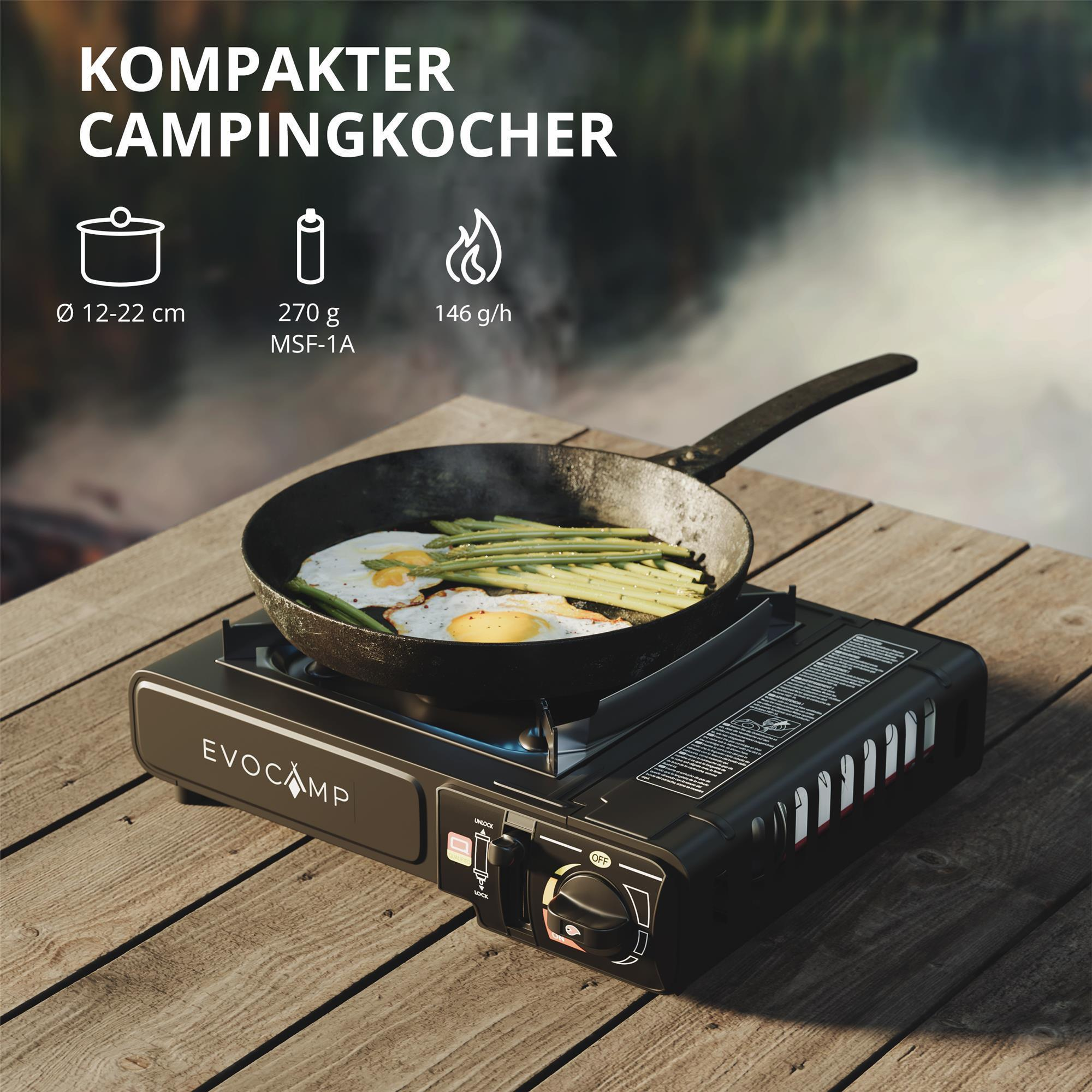 Ein Campingkocher mit Pfanne, in der Eier und Spargel gebraten werden. Holzoberfläche.