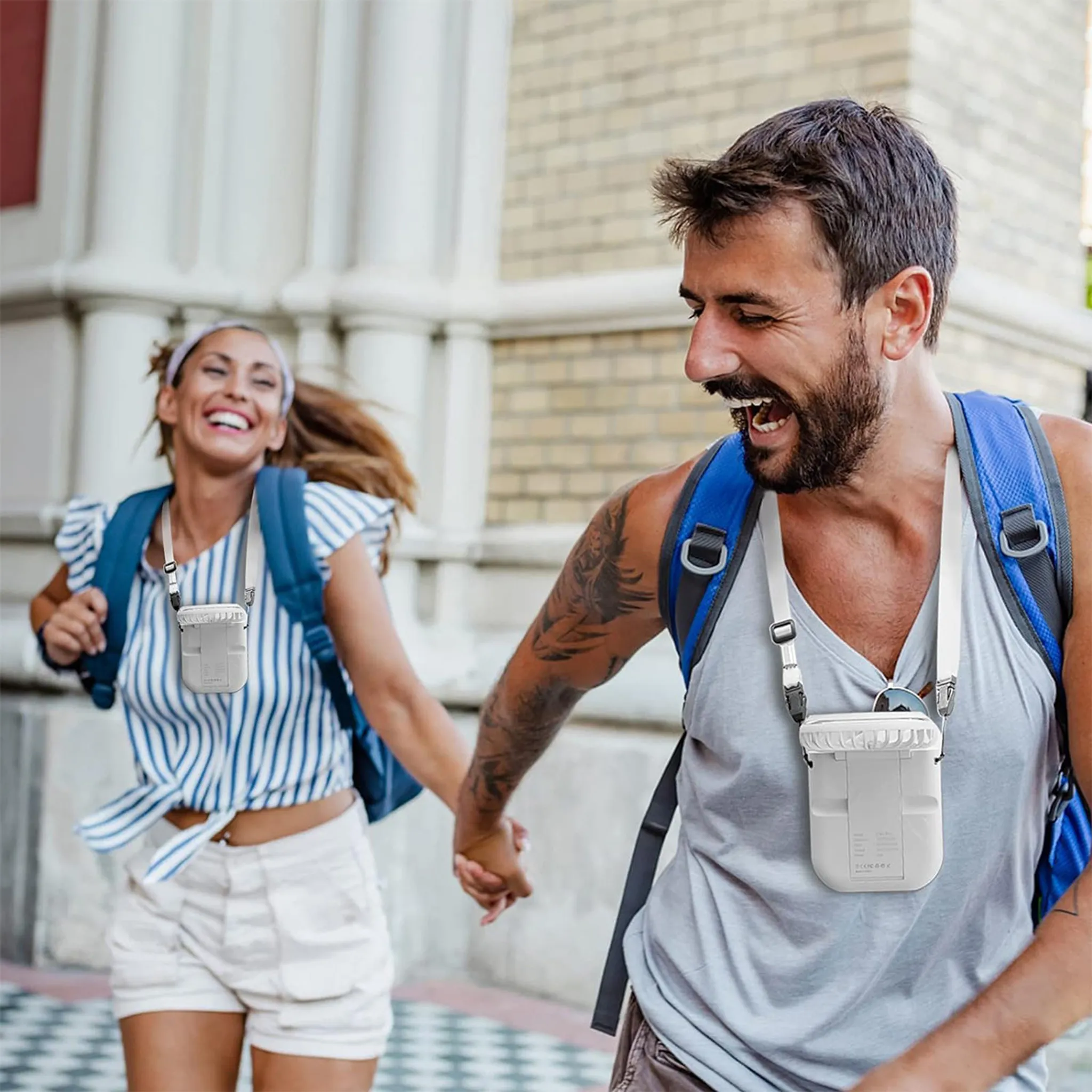 Mann und Frau mit Rucksäcken und Halsventilatoren laufen lächelnd und halten Händchen.