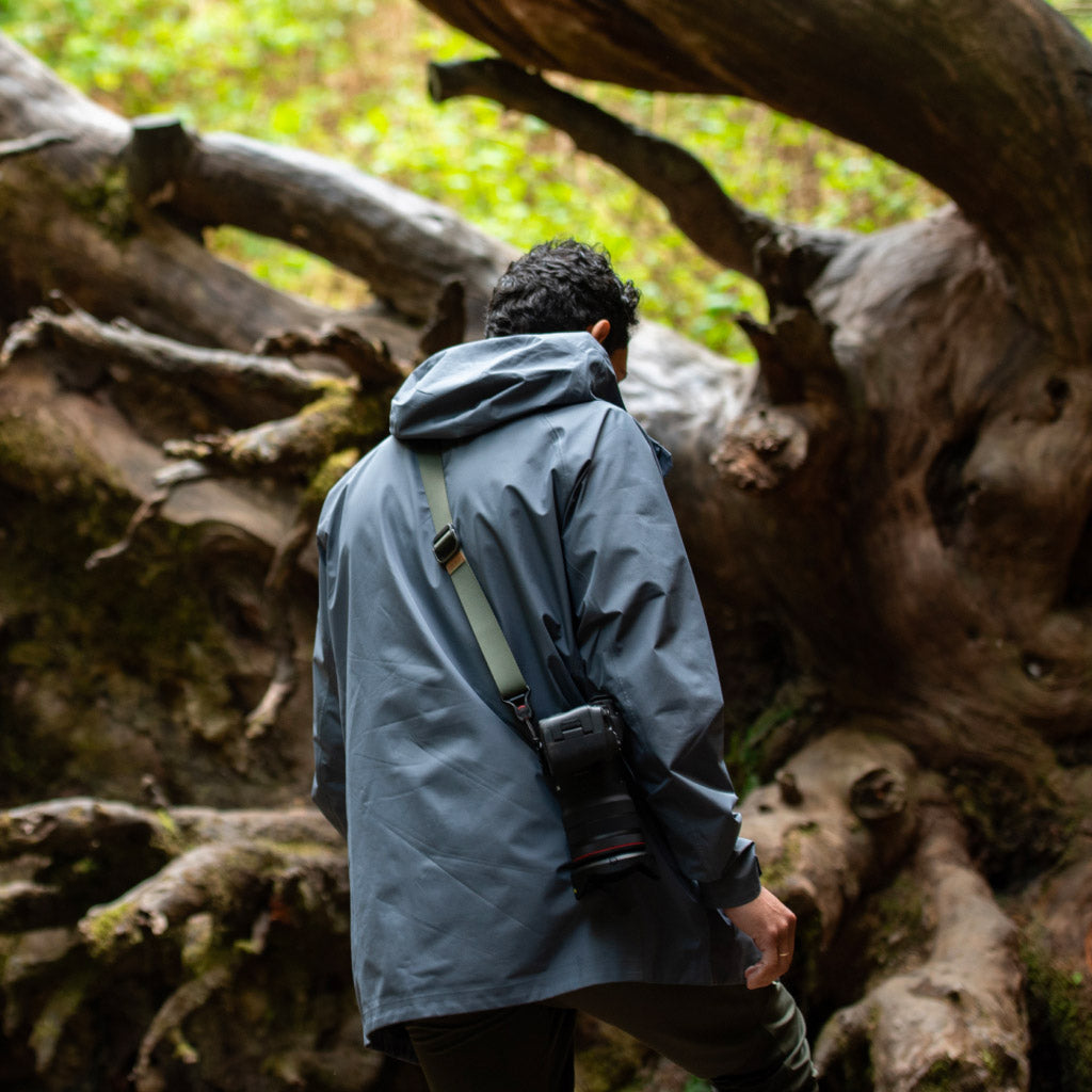 Uomo con macchina fotografica nel bosco, vicino a un tronco.