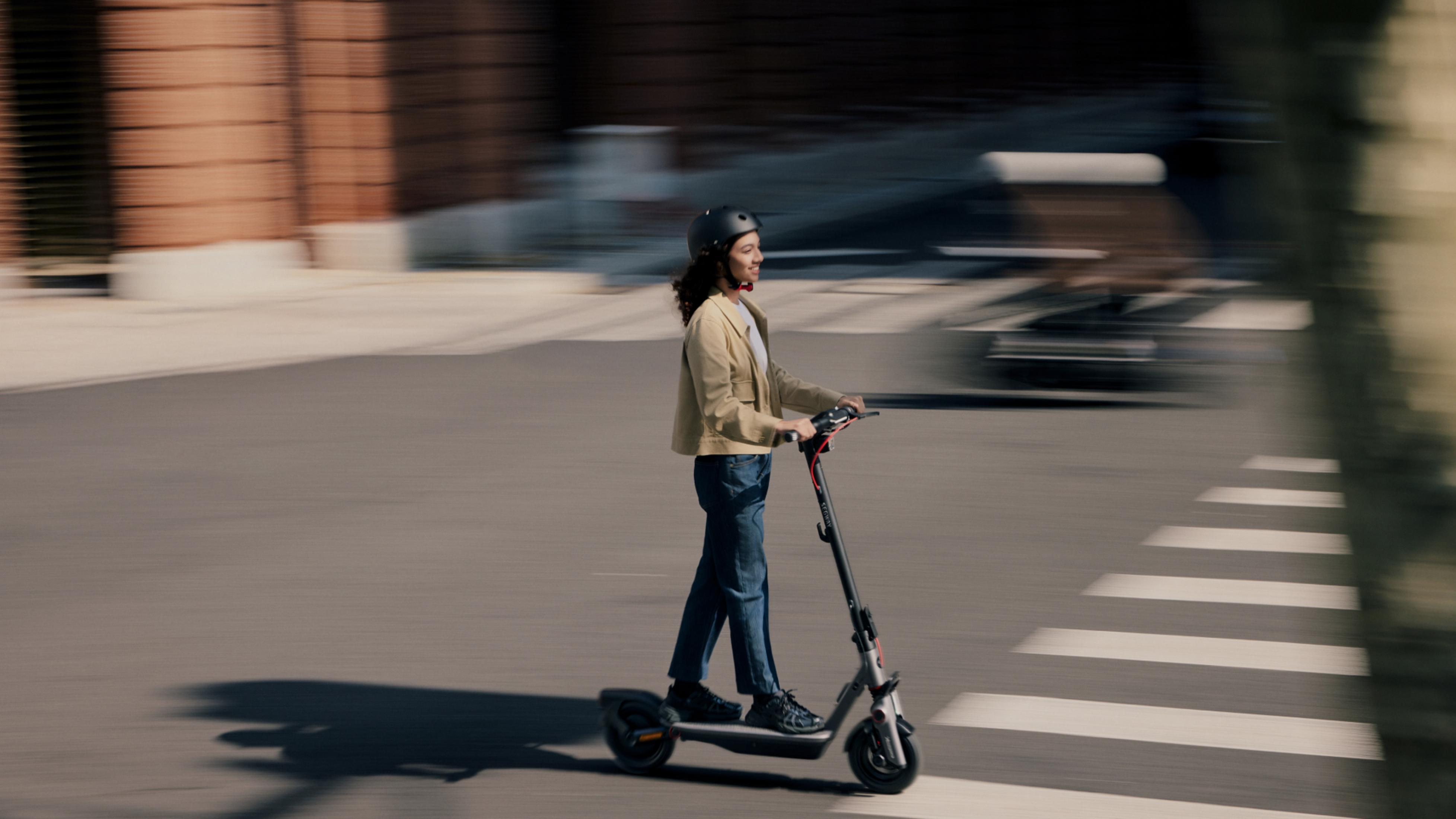 Eine Person fährt mit einem Elektroroller über eine Straße mit Zebrastreifen.