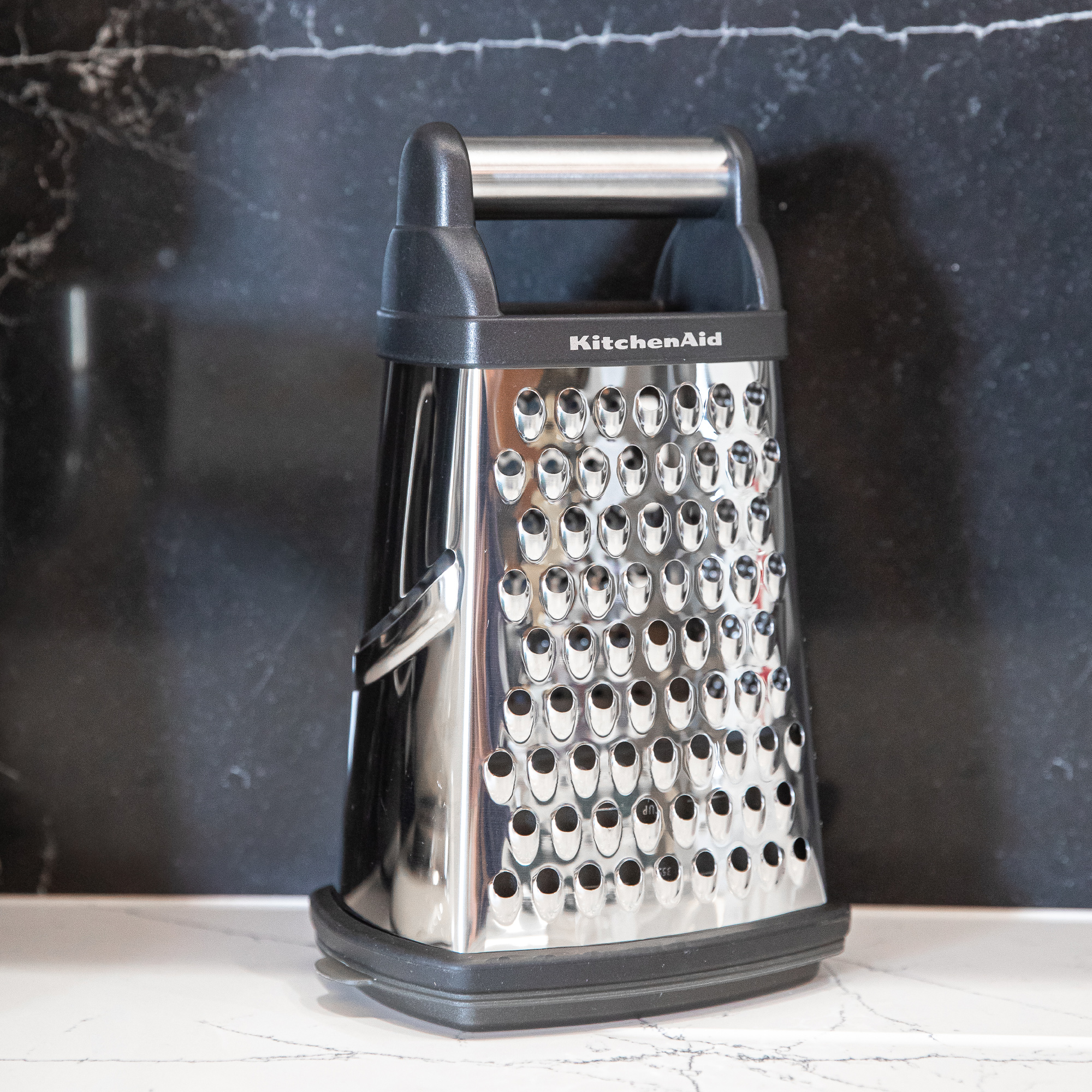 Ein KitchenAid-Reibe auf einer Marmorarbeitsplatte vor einem dunklen Hintergrund.