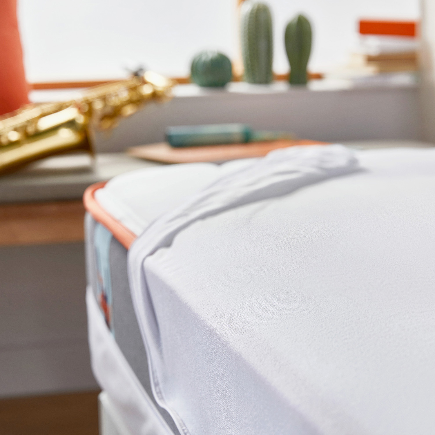 Un saxofón descansa sobre una cama con ropa de cama blanca. Decoración de cactus al fondo.