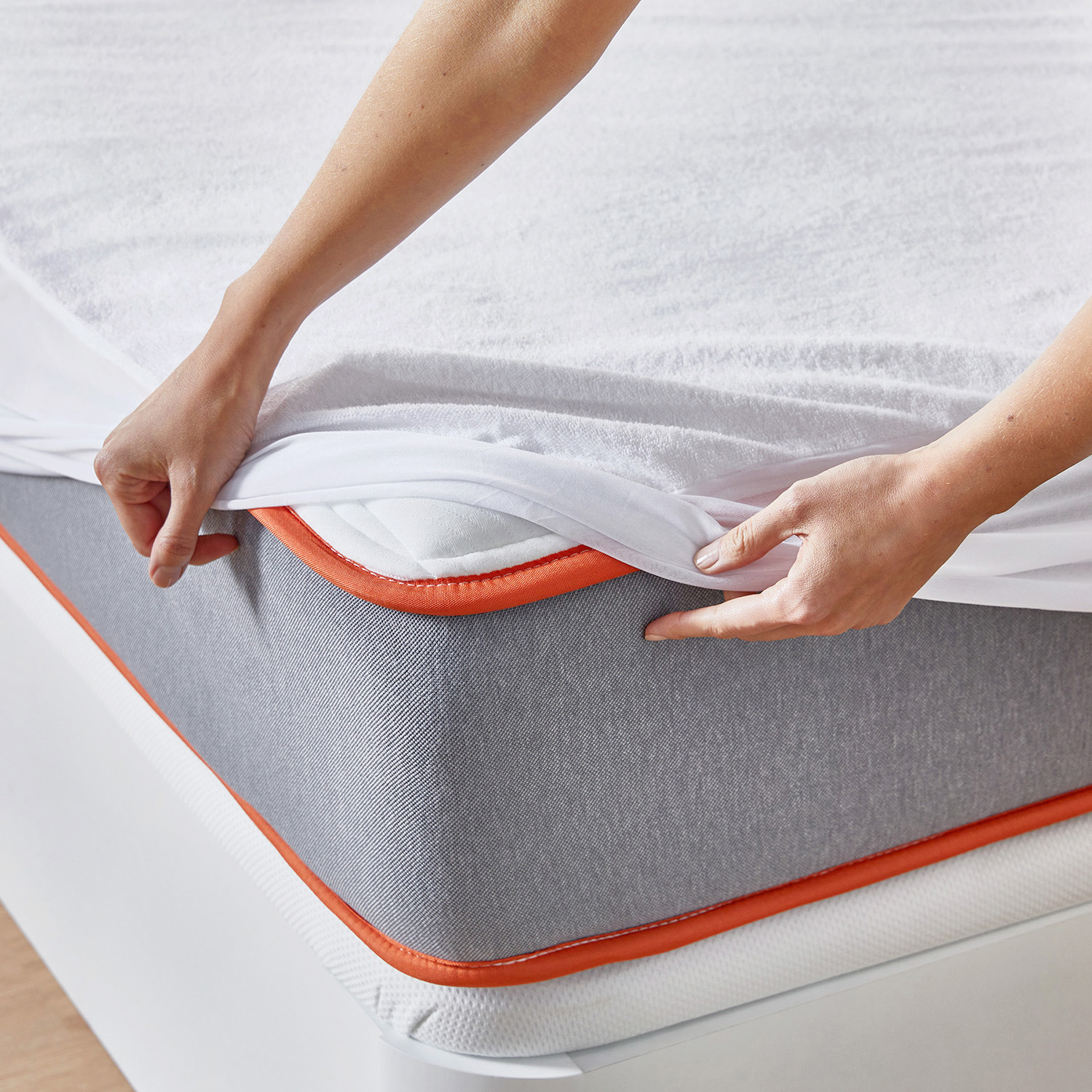 Manos ponen una funda blanca sobre un colchón gris con borde naranja.