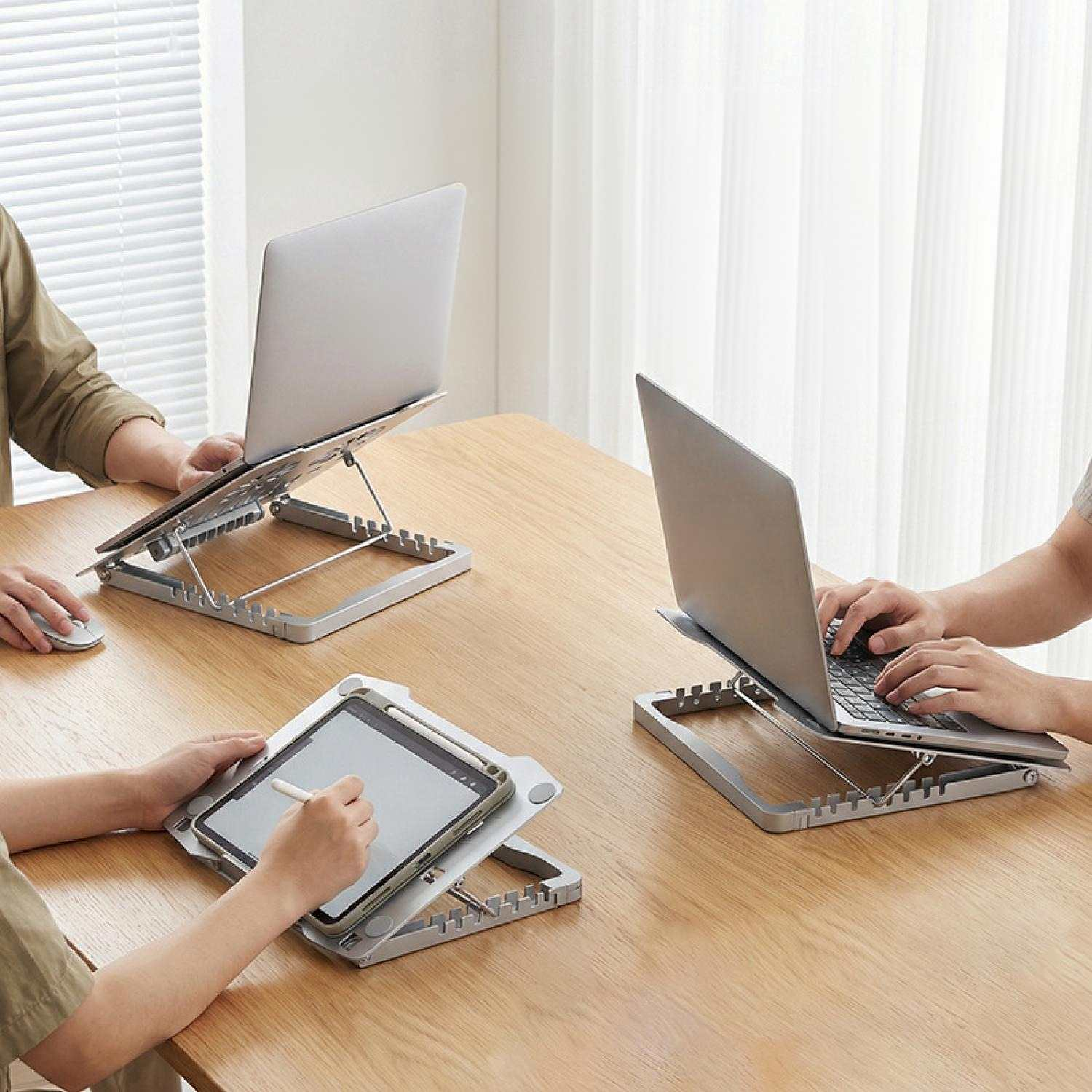 Drei Personen arbeiten an Laptops und Tablets auf höhenverstellbaren Ständern.
