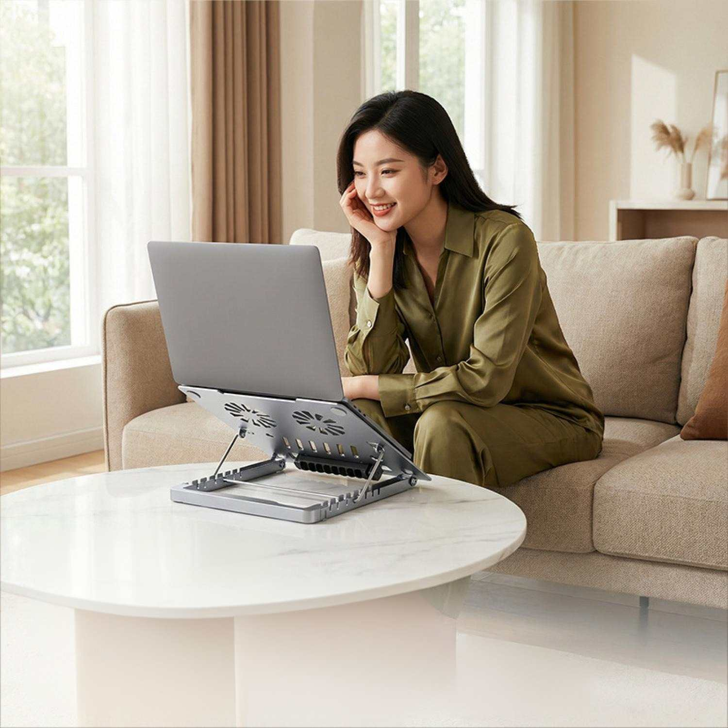 Eine Frau sitzt auf einem Sofa und arbeitet an einem Laptop auf einem Tisch.