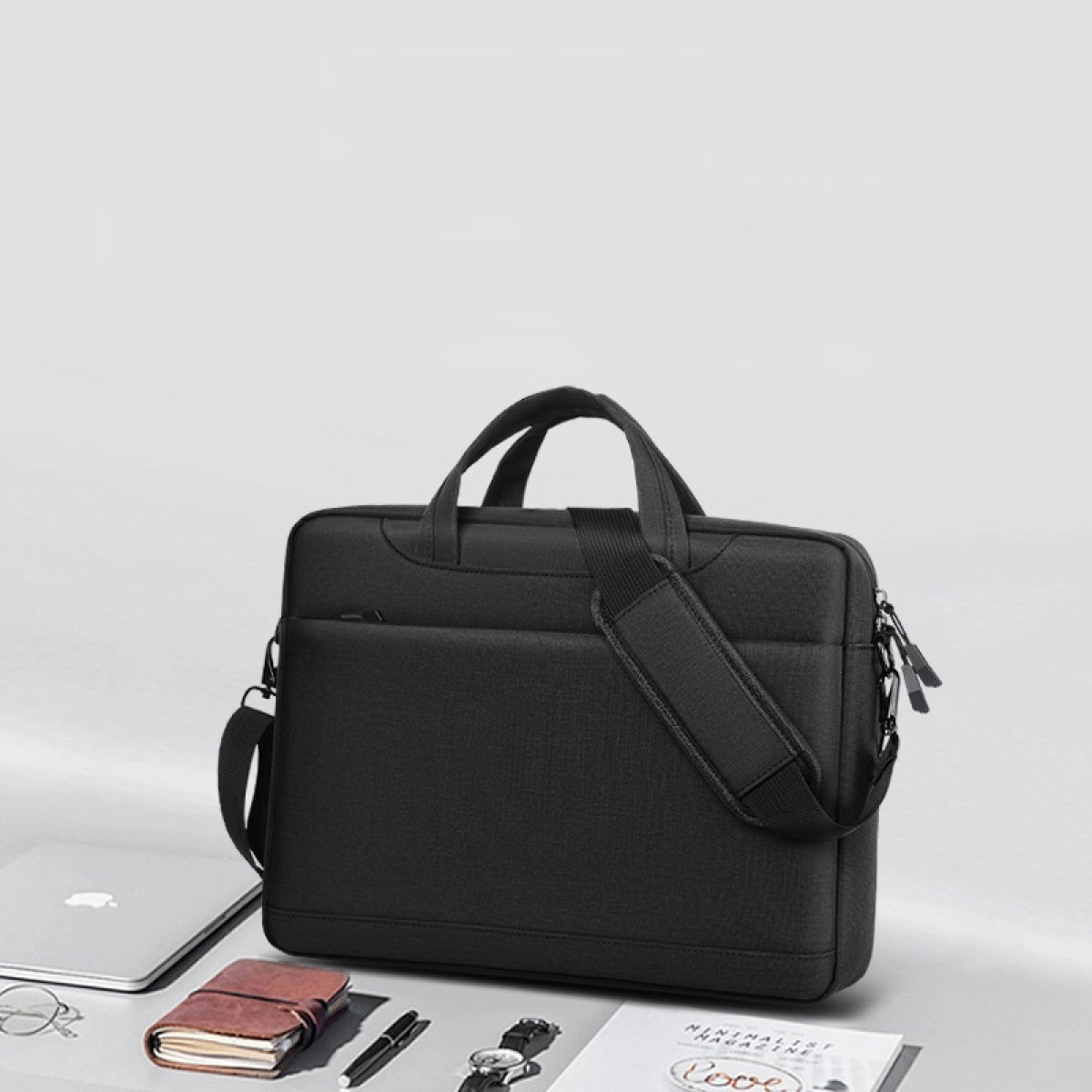 Schwarze Laptoptasche mit Henkeln und Schultergurt, neben Laptop und Notizbuch.