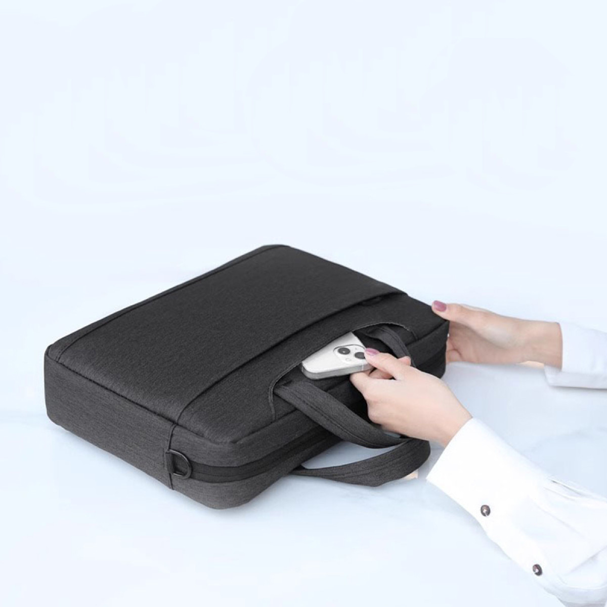 Eine Person steckt ein weißes Smartphone in die Tasche einer schwarzen Laptoptasche.