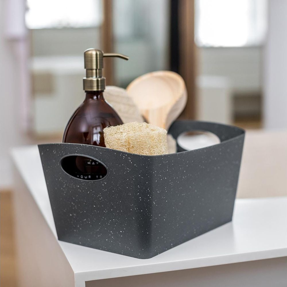 Ein dunkler Korb mit Seifenspender, Luffa und Holzschaufel.