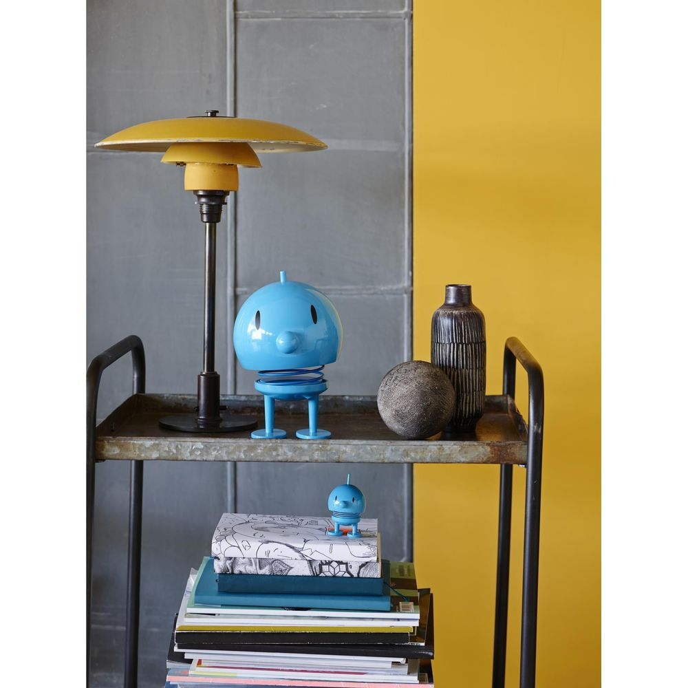Un robot a molla blu accanto a una lampada e una pila di libri.