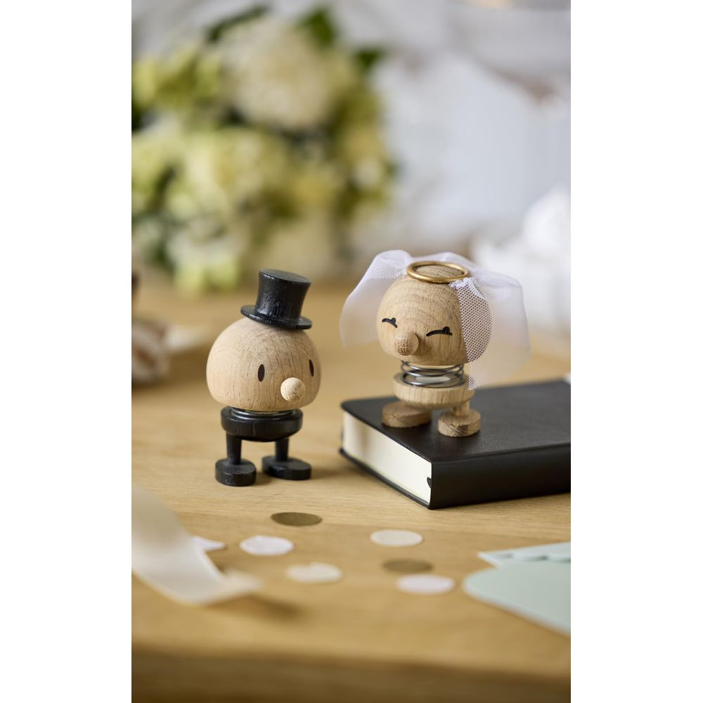 Figure di sposi in legno su un tavolo con coriandoli e fiori.