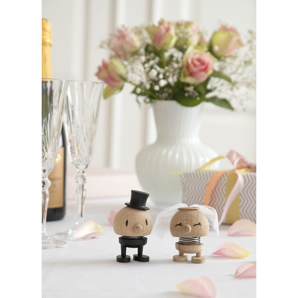 Figure di legno di sposi, champagne, bicchieri, regalo e rose rosa su un tavolo.