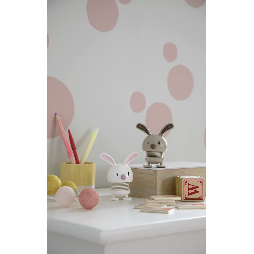 Due giocattoli coniglietto su scrivania con matite colorate e palline morbide. Muro con cerchi rosa.