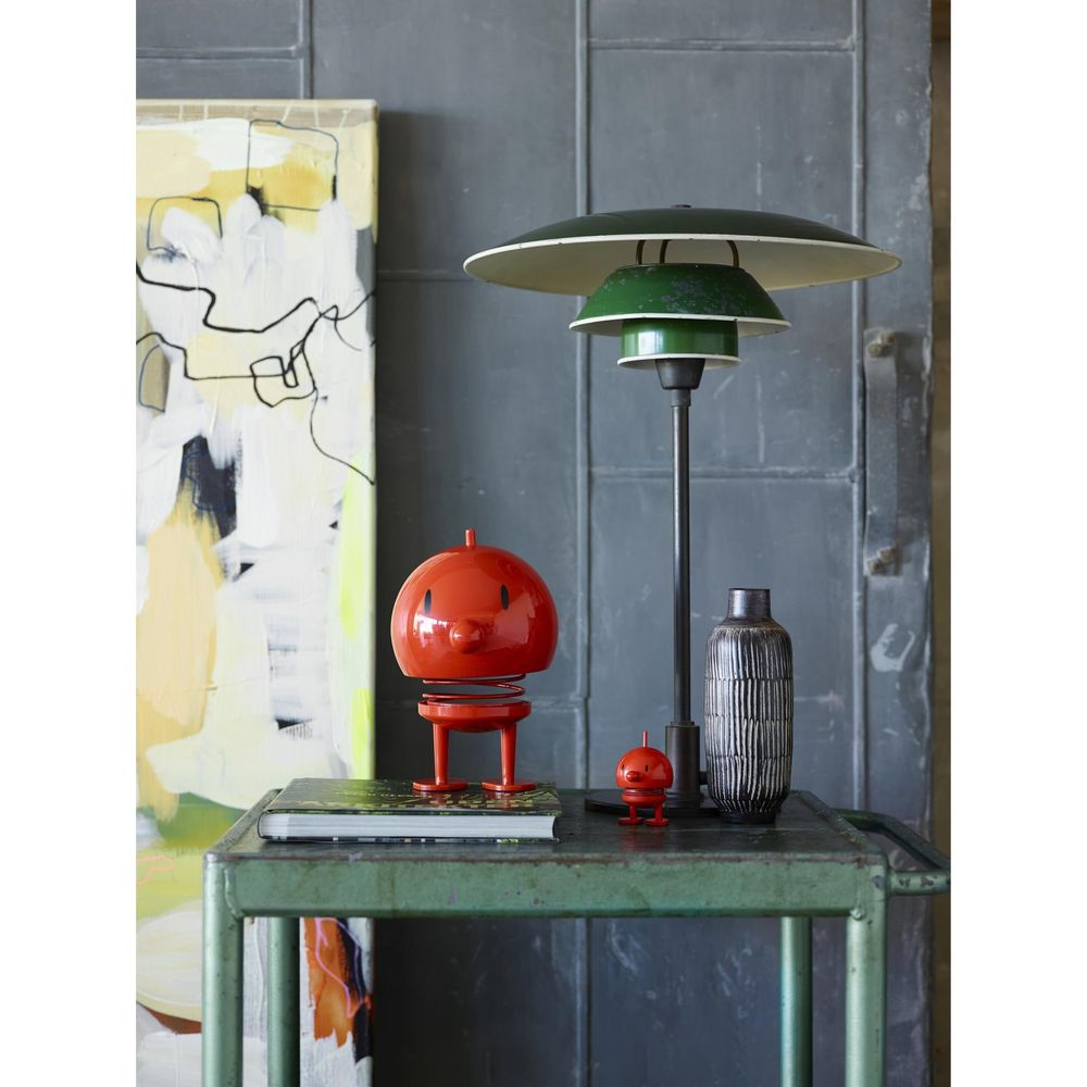 Una figurina di robot rossa siede su un tavolo accanto a una lampada verde e un vaso.