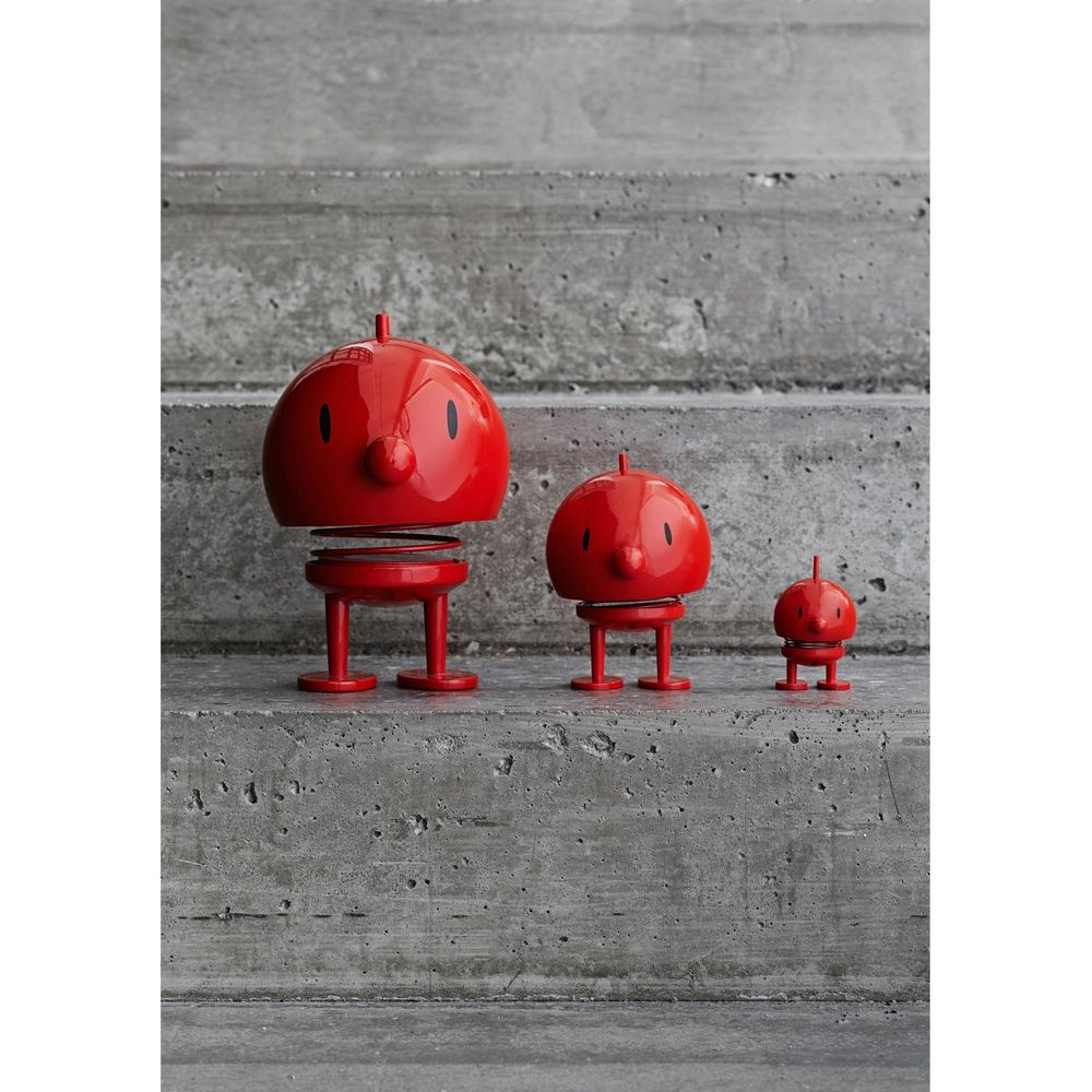 Tre figure rosse a molla su gradini di cemento.