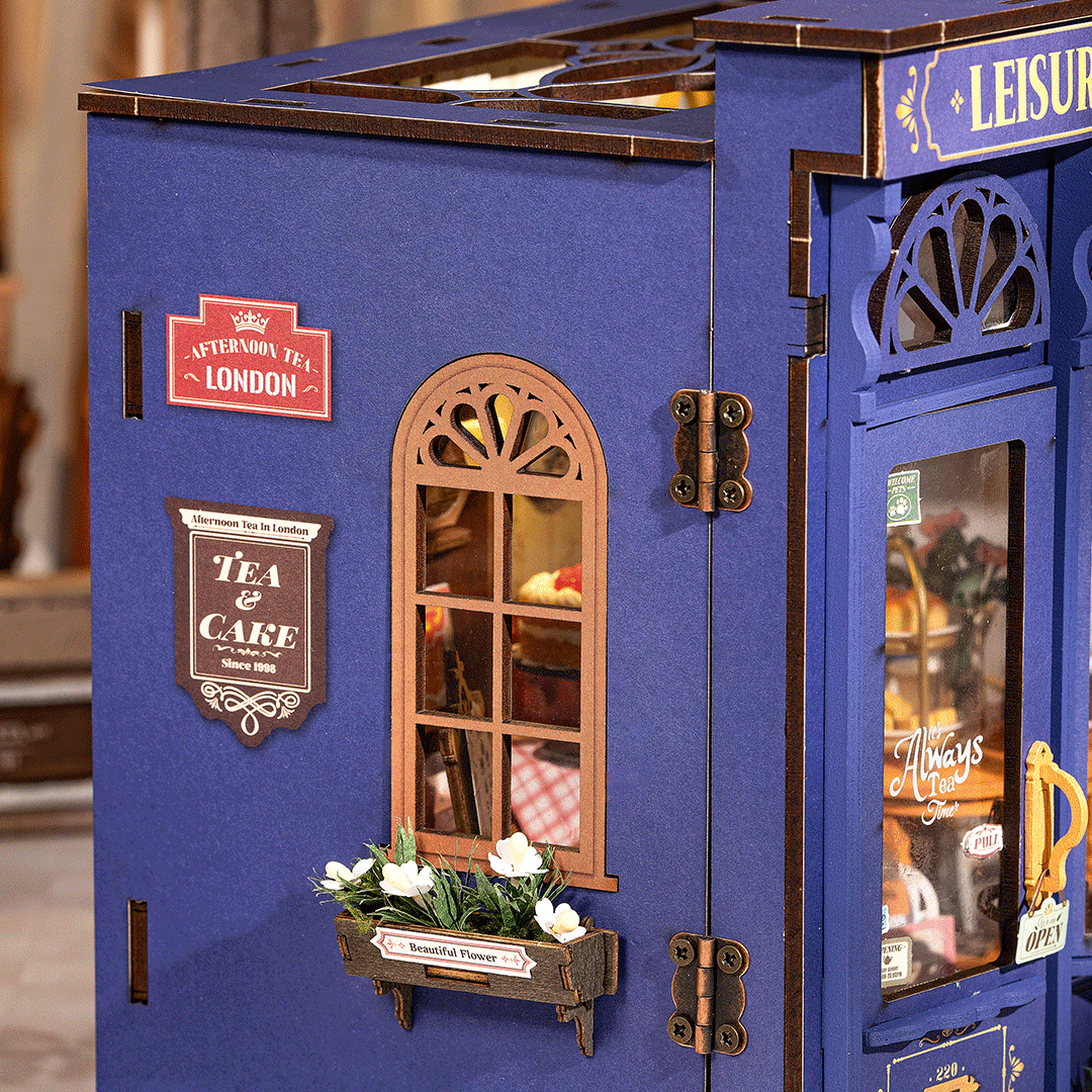 Ein miniatures blaues Gebäude mit Schildern für Tee und Kuchen, einem Fenster und Blumen.
