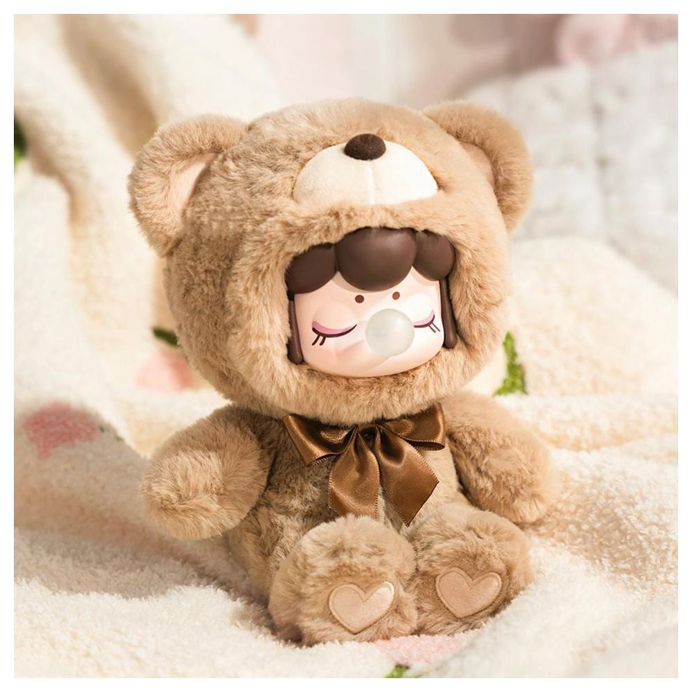 Une peluche ours en peluche marron avec un visage de fille soufflant une bulle est assise sur une couverture.