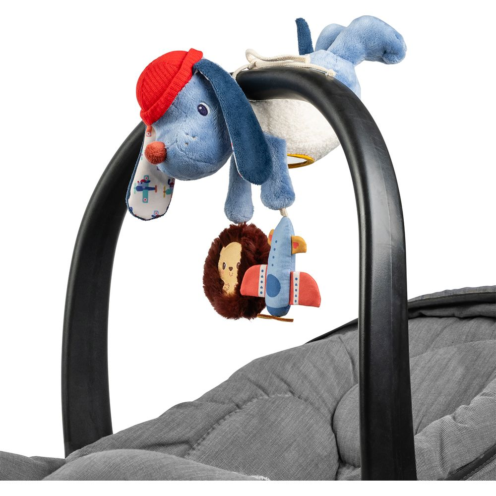 Un cane di peluche blu con cappello rosso pende da una barra del passeggino con giocattoli.