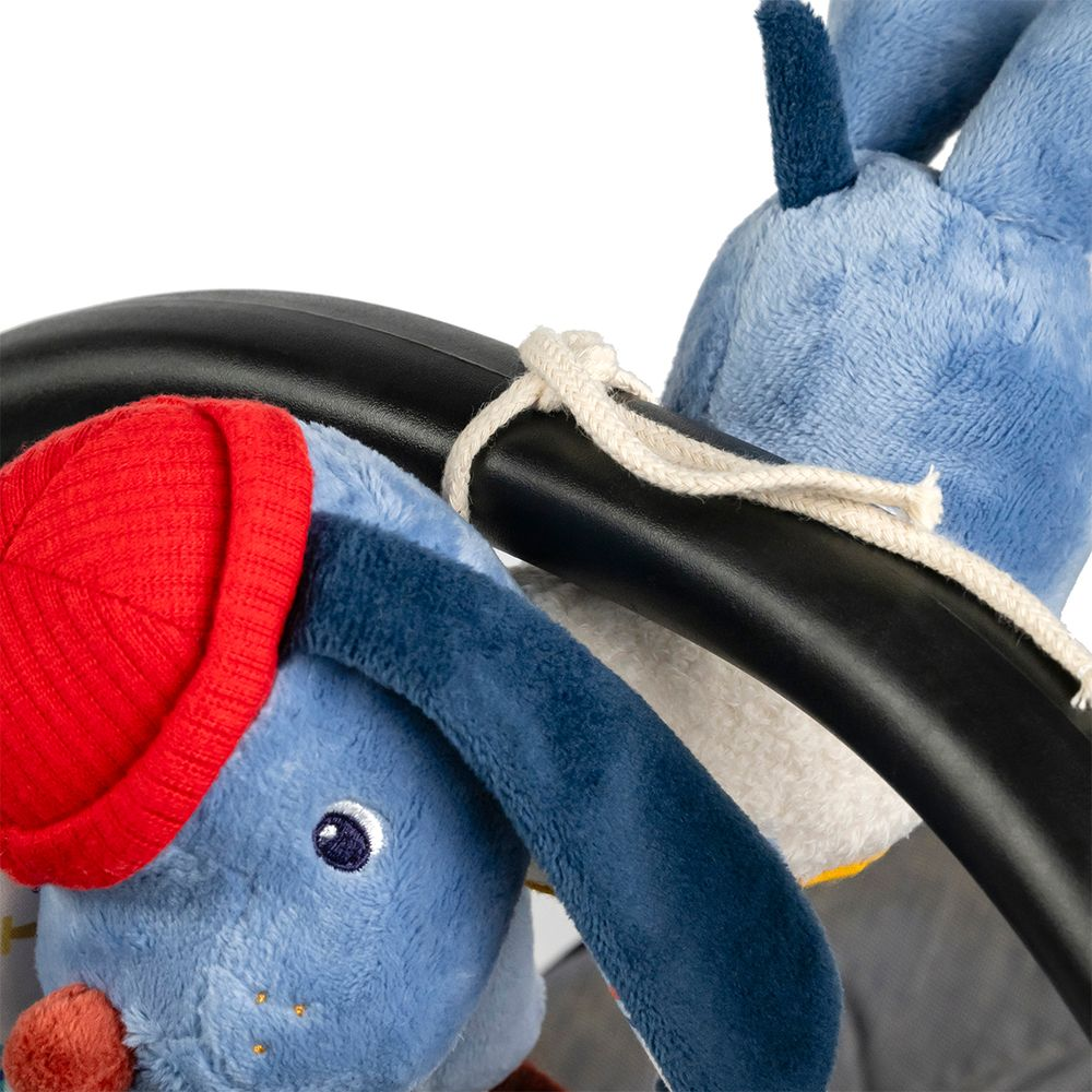 Due coniglietti blu di peluche, uno con cappello rosso, pendono da una barra nera, legati con corda.