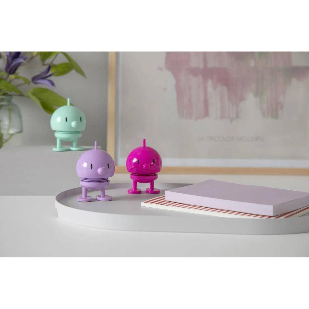 Drei bunte Figuren auf einem Tisch vor einem Bild und Blumen.
