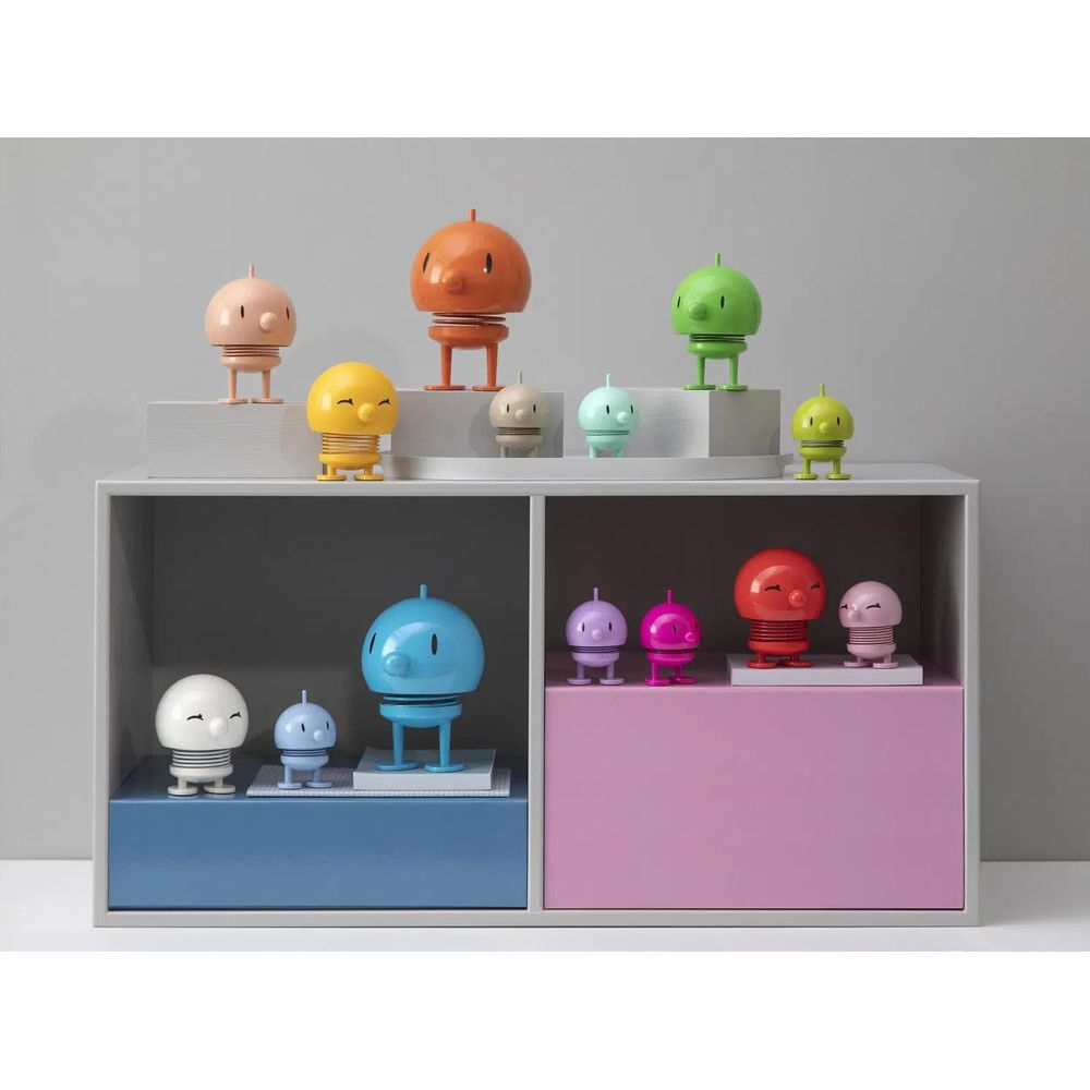 Mehrere bunte Figuren auf einem Regal. Sie sind hell und haben einen Kopf und Beine.