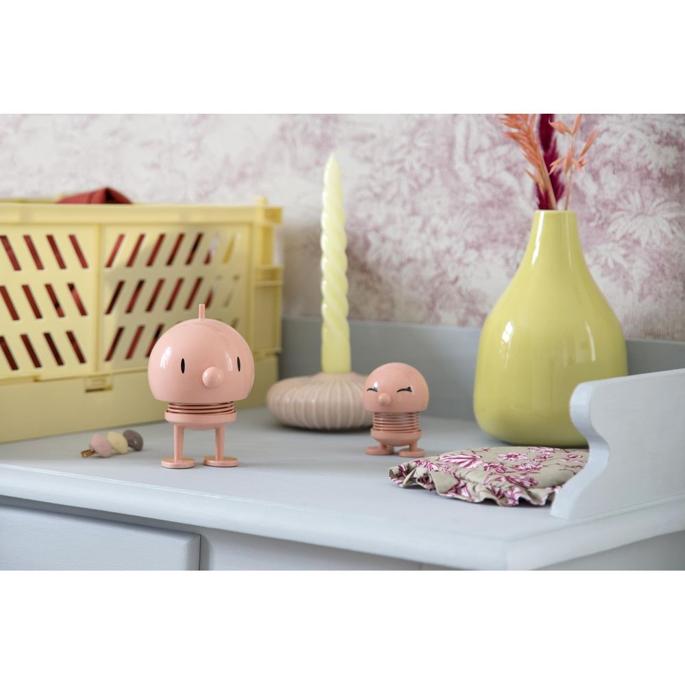 Due figure rosa dei cartoni animati si trovano su uno scaffale accanto a una cassa gialla, candela e vaso.