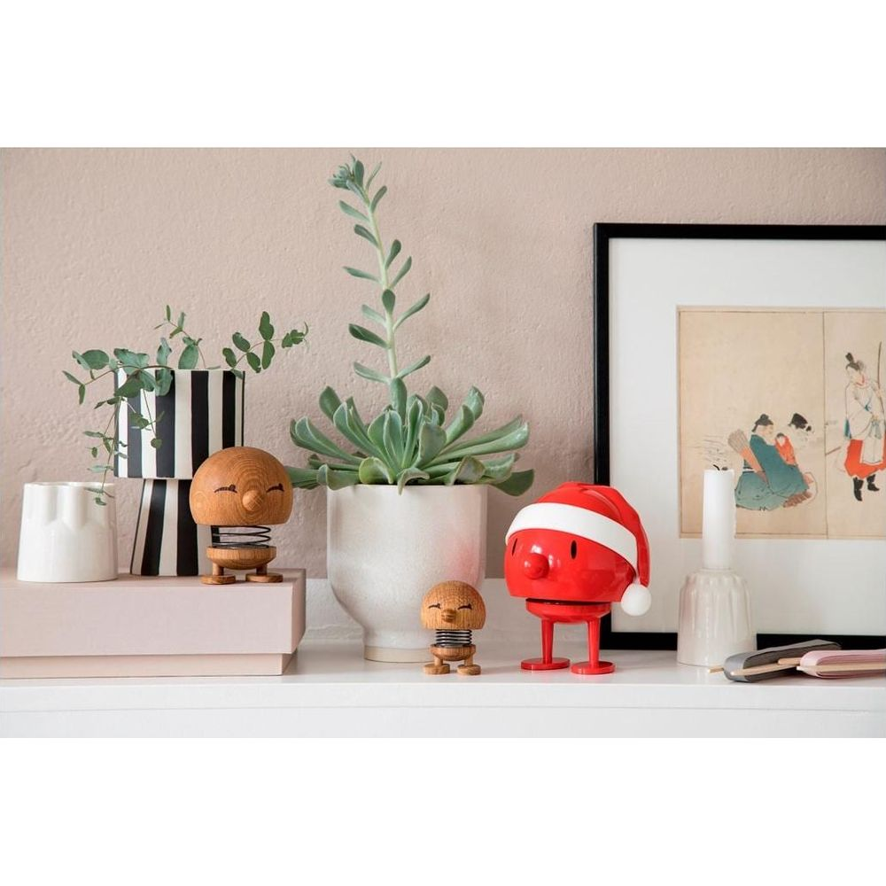 Decorazioni su uno scaffale: figure di legno, piante, una figura con cappello da Babbo Natale e arte.