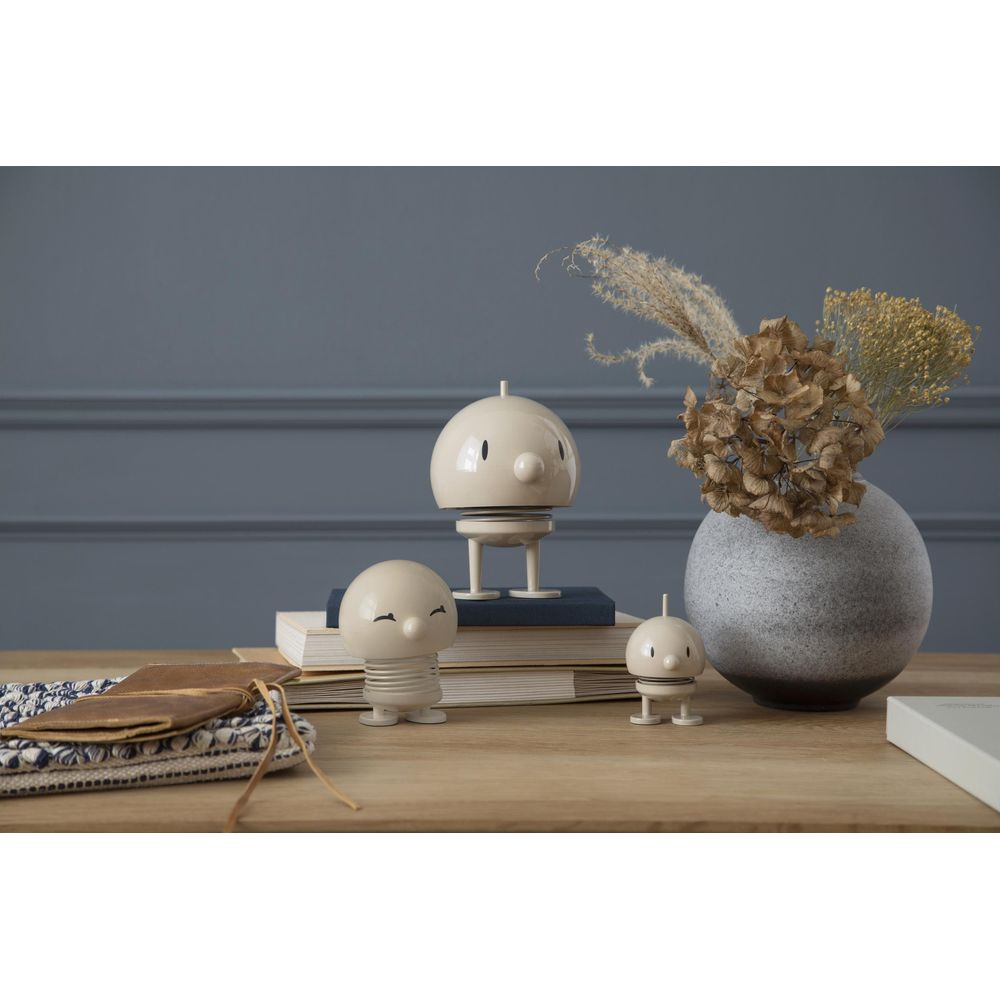 Tre figure bianche su un tavolo di legno con libri e un vaso di fiori secchi.