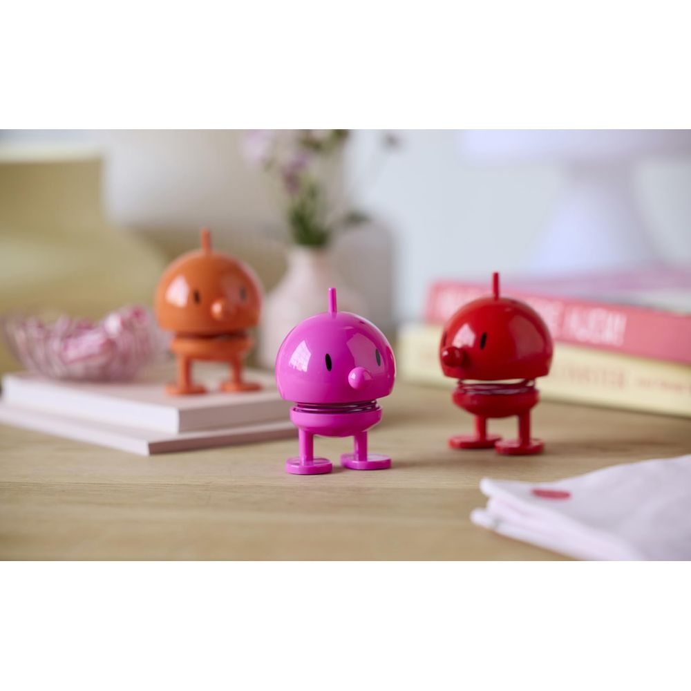 Drei kleine Springfiguren in Pink, Orange und Rot auf einem Holztisch.