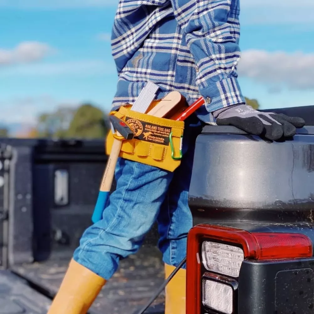 Ein Handwerker mit Werkzeuggürtel steht am Heck eines Pickups.