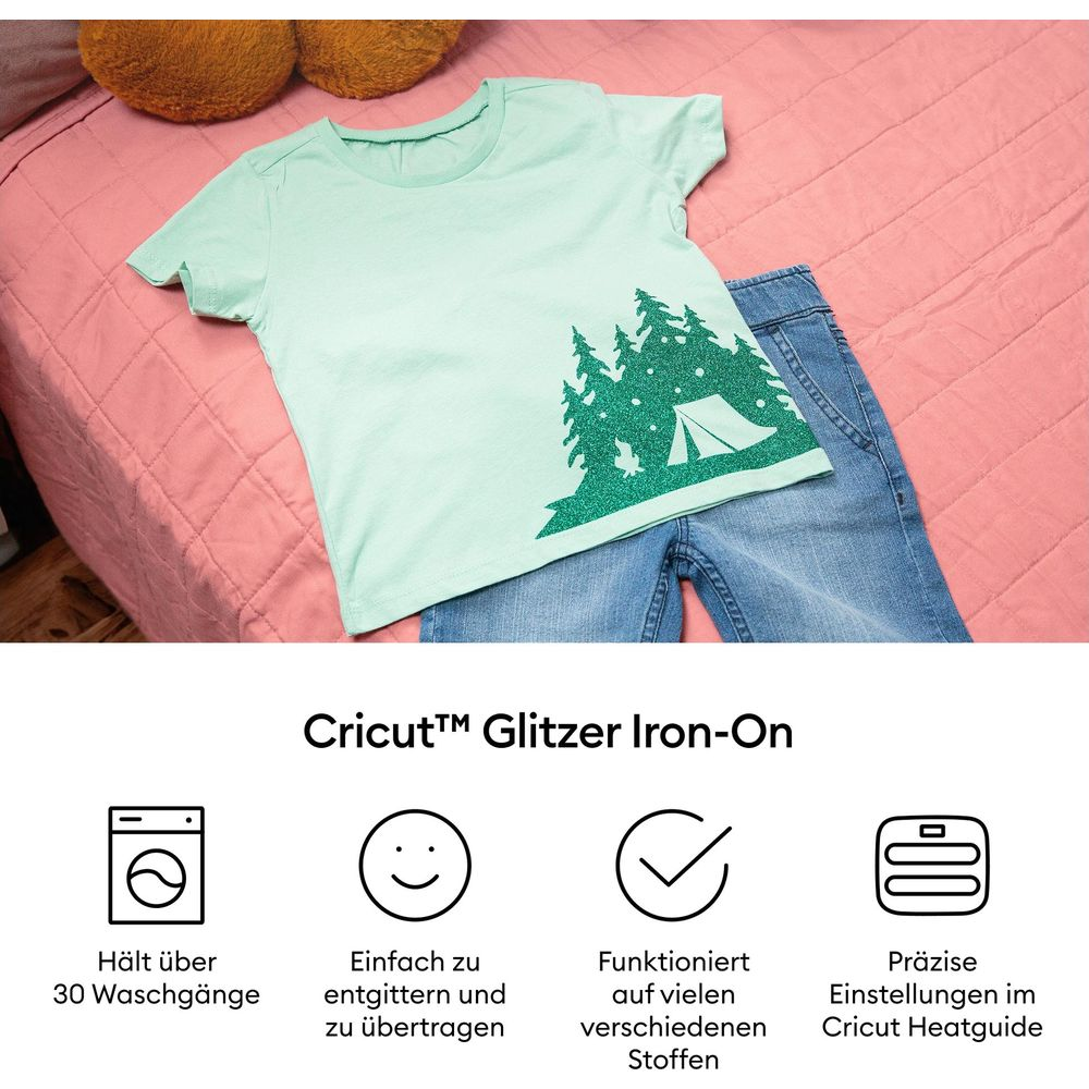 Hellgrünes T-Shirt mit glitzerndem grünen Wald und Zeltmotiv, liegt auf Jeans.
