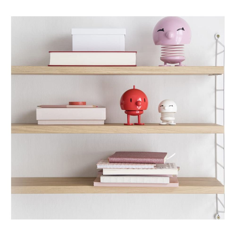 Tre mensole con oggetti decorativi: libri, scatole e figure. Accenti rosa e rossi.